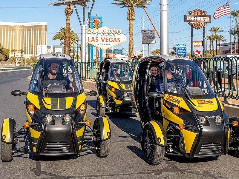 Three two-seat electric city cars lined up on the boulevard beside the Welcome to Fabulous Las Vegas sign