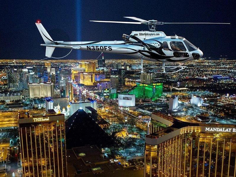 A sightseeing helicopter banking over the Las Vegas Strip at night, with the Luxor Sky Beam rising beside it
