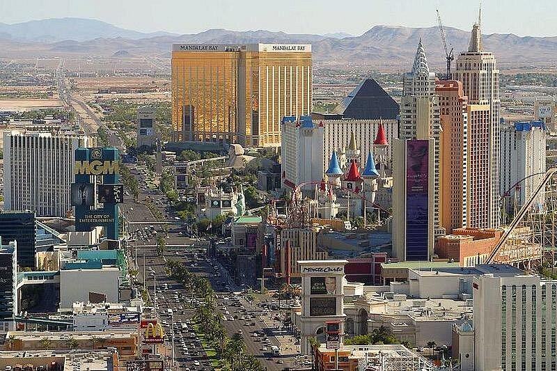 The Las Vegas Strip from the air in daylight, running south past Mandalay Bay and the Excalibur towers toward the mountains