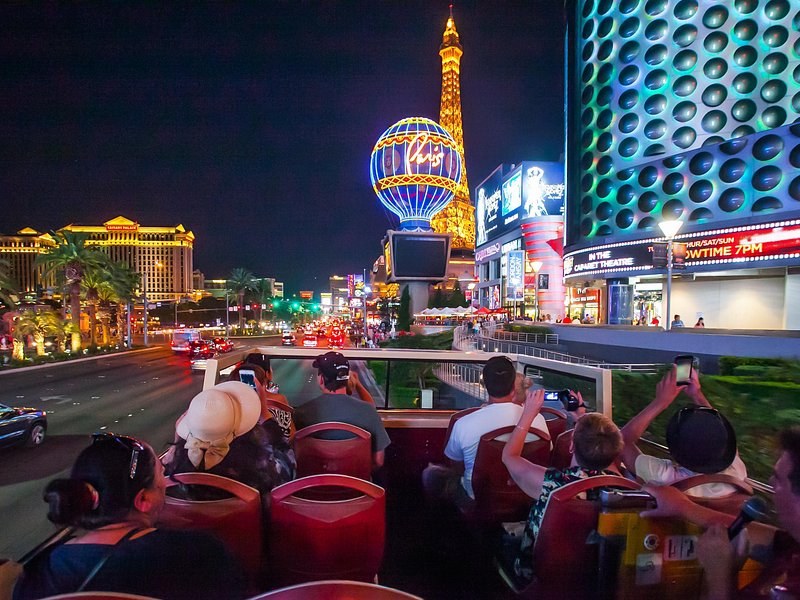 The open upper deck of a night sightseeing bus on the Las Vegas Strip, the Eiffel Tower at Paris Las Vegas lit up ahead