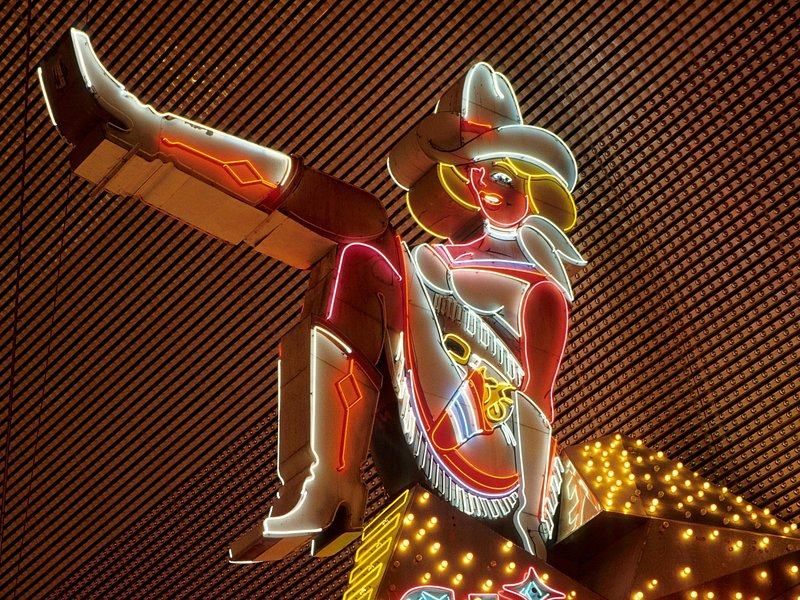 A restored neon cowgirl sign, one boot kicking, mounted on a brick wall in downtown Las Vegas